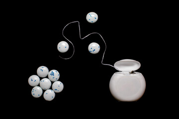 Dental floss and mint-flavoured round chewing gums on a black background. The concept of oral care and caries prevention. Modern dental care and human oral hygiene
