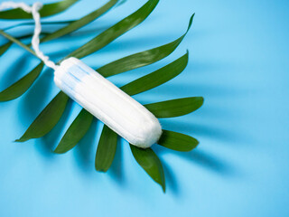 Clean white cotton swabs on a blue background on a green leaf. Feminine hygiene during menstruation, cosmetic procedures.