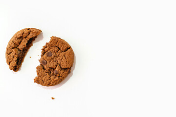One chocolate chip cookie broken into two pieces with crumbs on a white background and free space for text. Delicious homemade American cookies. Delicious sweet breakfast with milk for vegetarians