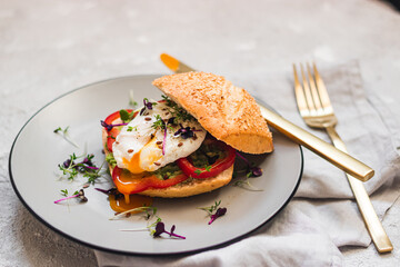 Poached egg on a bun with avocado, bell pepper and micro green on a gray plate. Healthy breakfast. Brunch idea. Clean eating. vegetarian. protein source food