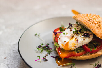 Poached egg on a bun with avocado, bell pepper and micro green on a gray plate. Healthy breakfast. Brunch idea. Clean eating. vegetarian. protein source food