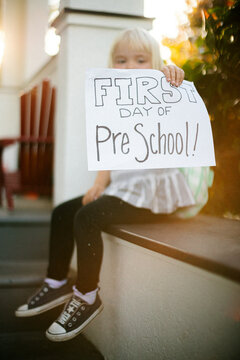 child holds a first day of preschool sign on a sunny morning