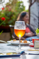 a glass of beer stands on a table in a cafe outside and glows from the sunlight. a woman sits in the background