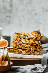 Healthy, natural summer food. Sandwiches with whole grain bread, prosciutto, figs and brie cheese on wooden board napkin on a gray background. Healthy snack. Food to go. Lunch. Brunch ideas