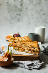 Healthy, natural summer food. Sandwiches with whole grain bread, prosciutto, figs and brie cheese on wooden board napkin on a gray background. Healthy snack. Food to go. Lunch. Brunch ideas