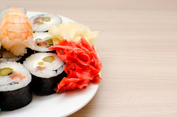 Various types of sushi and rolls next to ginger on a white plate. Place for text, copyspace.