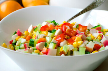 salad of fresh vegetables - cucumbers, bell peppers, corn and crab sticks in a white bowl on the table.