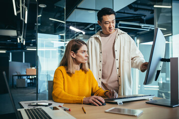 Two freelancers, an Asian man and a woman, work in a modern office, discussing and discussing a...
