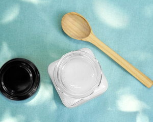 Coconut oil in an open glass jar on a blue background. Near the jar are a wooden spoon and a lid. Healthy food concept. Flat lay