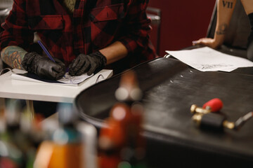 Process of transferring tattoo design onto transfer paper, photo of tattoo artist hands in black gloves drawing while sitting at table