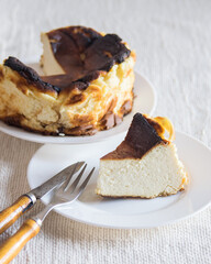 Basque Burnt San Sebastian Cheesecake with cutted piece on a white plate on light background, selective focus