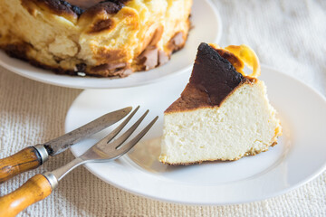 Basque Burnt San Sebastian Cheesecake with cutted piece on a white plate on light background, selective focus
