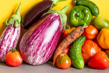Organic vegetables healthy vegetarian food concept. Farm aubergine eggplants, tomatoes of various grade, bell peppers, carrot and cucumber on a yellow gray background