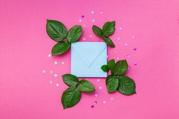 kraft blue envelope surrounded by confetti stars and fresh leaves on a pink color paper background. Mother's Day, Easter, Valentine's Day, holiday concept. Flat lay.