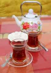 Two Glasses of Hot Turkish Tea with Blurry Teapot and Sugar Cubes in the Backdrop