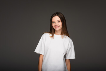 Obraz premium pretty woman in white t-shirt smiling at camera isolated on dark grey