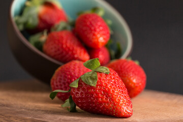 strawberries falling from a bowl onto a wooden board