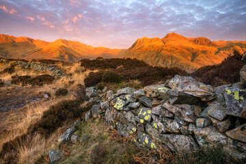Stone wall at Side Pike with golden light at sunrise on Langdale mountains in the Lake District, UK. 
