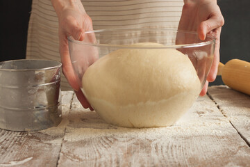 A woman holds a glass cup with a dough in her hands.
