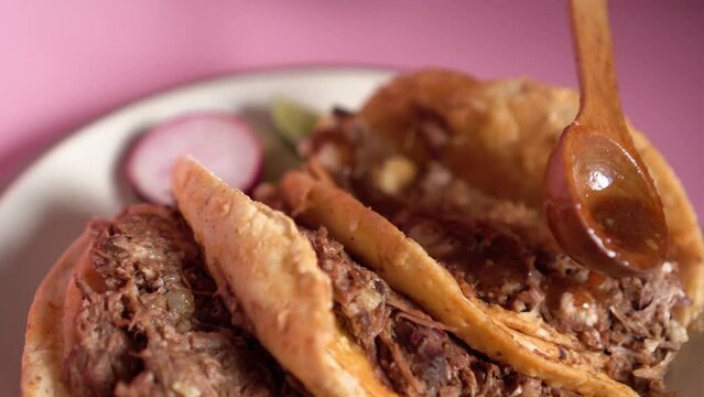 a person putting salsa on his guadalajara-style birria tacos with mexican ingredients and flavors
