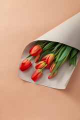 Bouquet of red tulips with kraft paper  on a natural beige color background. Mother's Day, Easter, Valentine's Day. Spring flowers. Copy space. Flat lay.