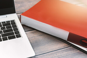 Red folder with place for text. Laptop computer on wooden table