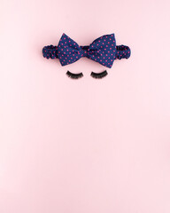 Blue hair bow tie with red spots. Big eyelashes. Woman's face composition. Rose background. 
