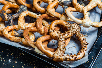 Fresh prepared homemade soft pretzels. Different types of baked bagels with seeds on a black background.