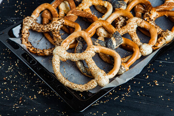 Fresh prepared homemade soft pretzels. Different types of baked bagels with seeds on a black background.