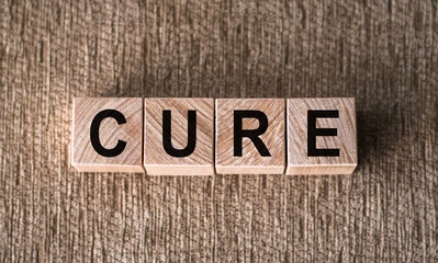 Fototapeta premium Word CURE made of wooden cubes on wooden background. Medical concept of treatment, prevention and side effects.