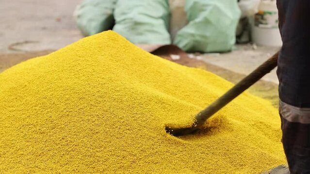 A worker stirs yellow rubber mulch with a shovel before placing it in a mixer to mix it with adhesive and lay it on the surface. Photo in motion. Selected Focus