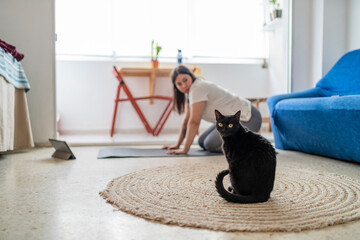 Chica joven guapa haciendo ejercicio en su casa con un gato negro