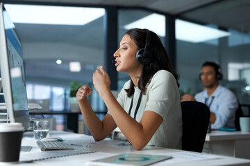 Hang in there, help is on the way. Shot of a young woman using a headset and computer in a modern...