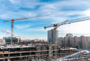 Fototapeta na wymiar Construction cranes at a construction site in the city against the blue sky in winter conditions. The concept of building a new area. Construction of a new building.