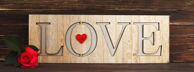 Love word written on wooden background and red rose