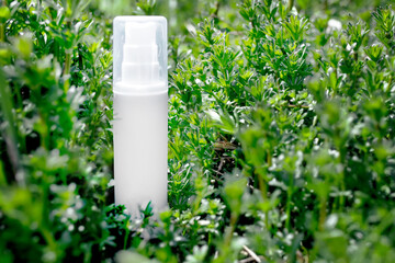 White unbranded dispenser bottle in meadow of flowers Galium aparine cleavers, clivers, goosegrass sticky willy, stickyjack, stickeljack, grip grass. MockUp bottle of shampoo