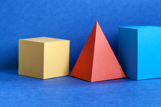 Multicolor geometrical figures still life composition. Three-dimensional prism pyramid rectangular cube objects on blue background. Platonic solids figures, simplicity concept