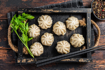Momo dumplings in a wooden tray with herbs. Dark Wooden background. Top view