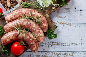 Bratwurst or sausages with spices and greens on a cutting board. On a white wooden table.
