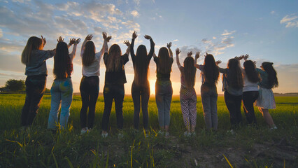 Silhouette of friends of 11 girls waving their hands at sunset in the field.