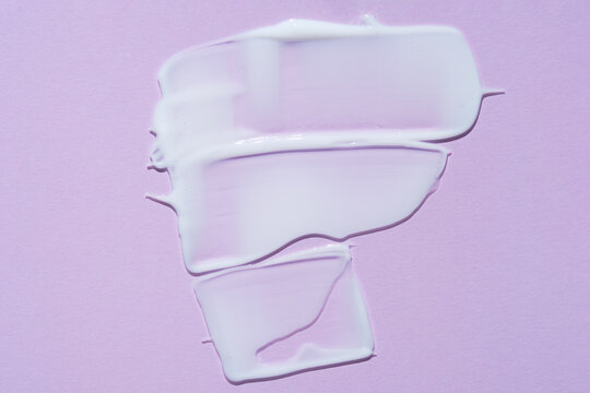 The texture of a facial skin care product. Smears of white cream with shimmer effect on a lilac background. Anti-aging anti-wrinkle care