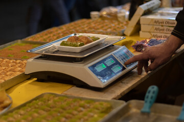 Old man hand weighing Turkish baklava with green pistachio on electronic scale. His face is not seen. Unrecognizable person. Turkey market, middle eastern cuisine. 