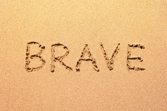 Brave word abstract written in the sand beach. Having courage motivational message