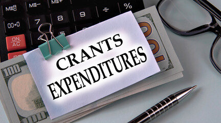 GRANTS EXPENDITURES - words on a white piece of paper fixed on banknotes against the background of a calculator, glasses and pen