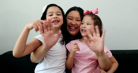 Obraz premium Asian mother waving hello to camera holding multi-ethnic little girls