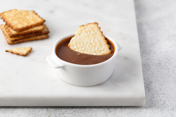 Crackers or cookies in chocolate paste in white sauce pan on marble background.