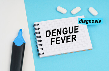 On a white and blue surface are pills, a marker and a notebook with the inscription - DENGUE FEVER