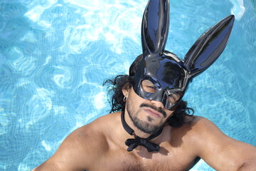 Seductive shirtless muscular man wearing bunny mask in swimming pool
