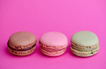 three colored macaroons on pink background with copy space