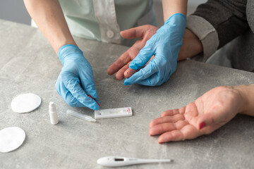senior woman hands using lancet on finger at home to check blood sugar level, glucometer and sugar cubes on wooden table close up, diabetes concept, elderly health care, sunny morning